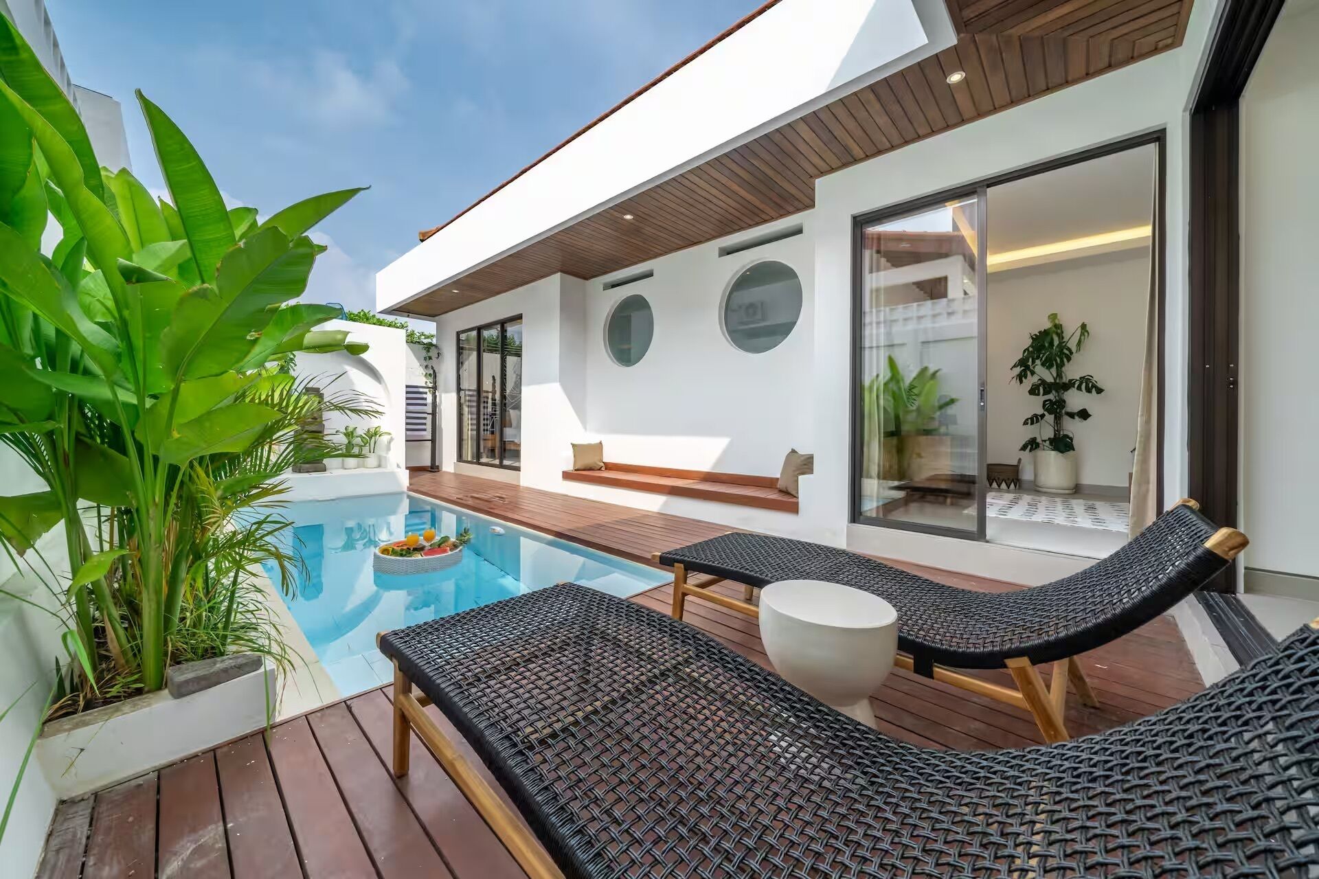 Un área de piscina moderna al aire libre con sillones de descanso, una terraza de madera y plantas en macetas.