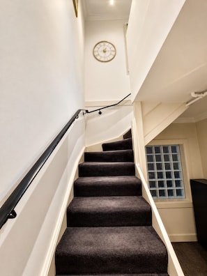 A staircase with a black handrail, carpeted steps, and a wall-mounted clock. - Cityside Comfort LOFT- Chippendale (Chippendale)