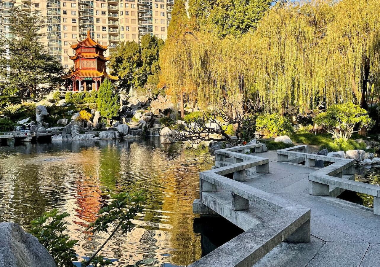 Un parque tranquilo con un pabellón tradicional, un puente de piedra y un estanque.