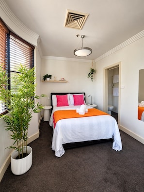 A hotel room with a bed, bedside tables, a hanging plant, a ceiling vent, and a bathroom door. - Cityside Comfort LOFT- Chippendale (Chippendale)