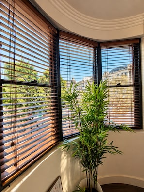 A corner room with two windows featuring horizontal blinds, a potted plant, and a framed picture on the wall. - Cityside Comfort LOFT- Chippendale (Chippendale)