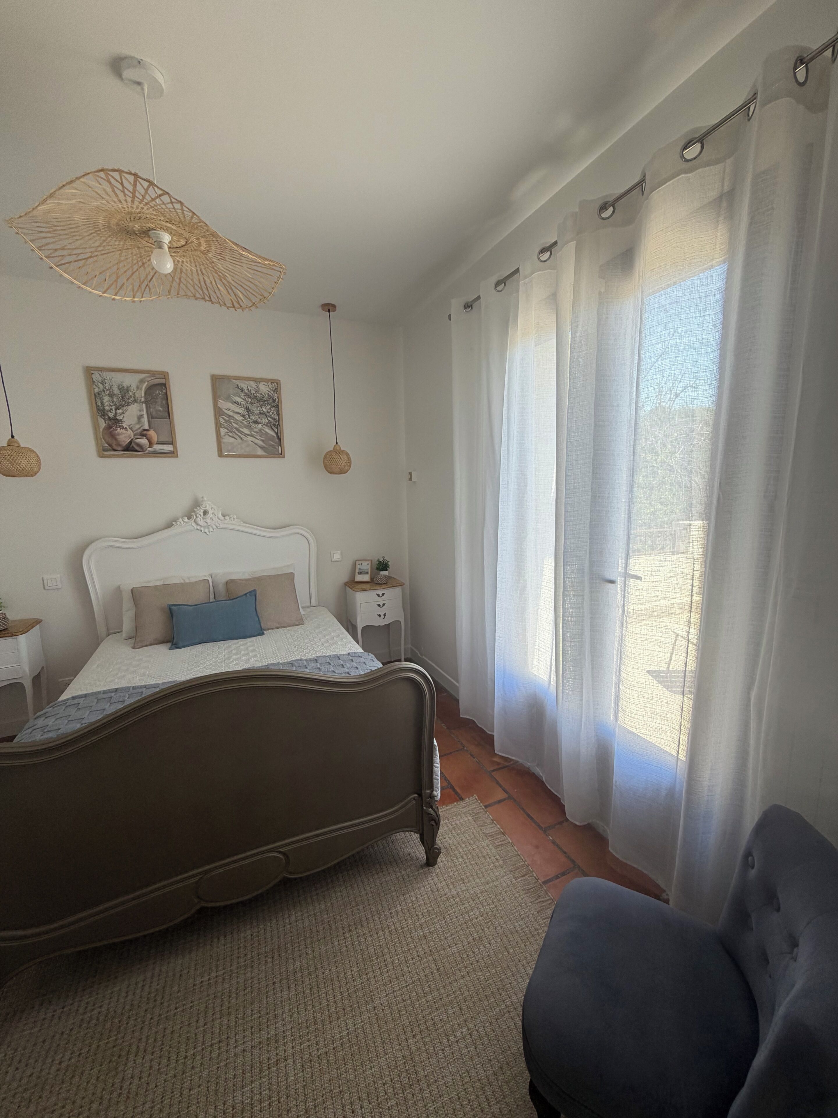 Ein Schlafzimmer mit Bett, Nachttisch, Stuhl, Pendelleuchte und einem fenster mit Vorhängen.