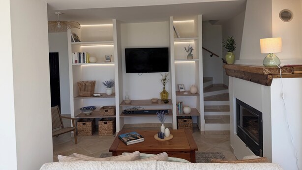 Ein Wohnzimmer mit Fernseher, Bücherregalen, Kamin und Treppe.