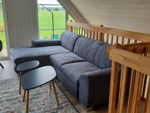 Ein modernes Wohnzimmer mit einem grauen Ecksofa, einem kleinen runden Tisch und einer Holztreppe.