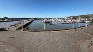 Un puerto deportivo con barcos amarrados, un paseo marítimo pavimentado y un cielo azul despejado.