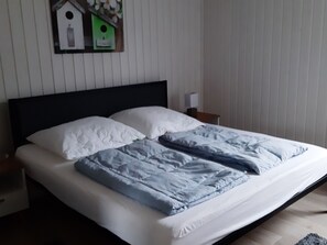 Ein Bett mit weißblauer Bettwäsche, einem Holz-Kopfteil und einem Nachttisch mit Lampe.