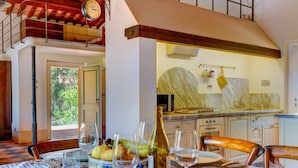 Uma área de refeições com uma mesa posta para uma refeição, uma cozinha ao fundo e um relógio na parede.