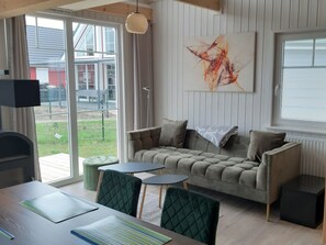 Ein modernes Wohnzimmer mit einer Couch, zwei Sesseln, einem kleinen Tisch und einem großen Fenster.