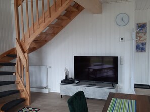 Ein Wohnzimmer mit Holzentreppe, Flachbildfernseher, Esstisch und einer Wanduhr.