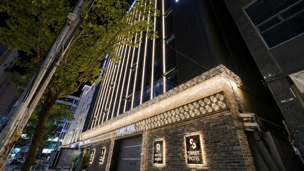 Un edificio con un letrero que dice 'SWEET HOTEL', un cartel de estacionamiento y fachada de ladrillo.