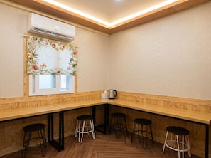 A corner room with a wooden counter, four stools, an air conditioning unit, and a floral-patterned window.