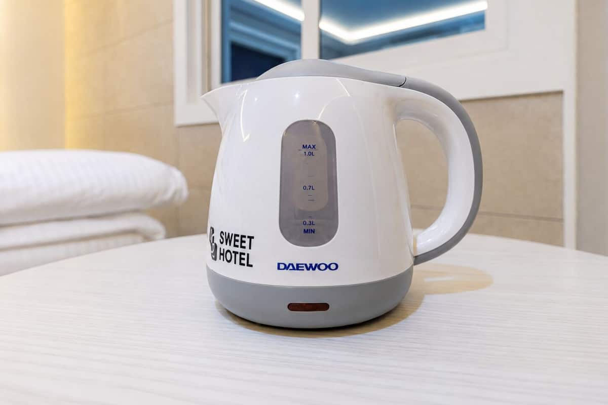 A white electric kettle with a digital display on a table in a hotel room.