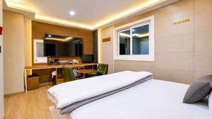 Habitación de hotel con cama, escritorio con computadora, silla, televisor y ventana.