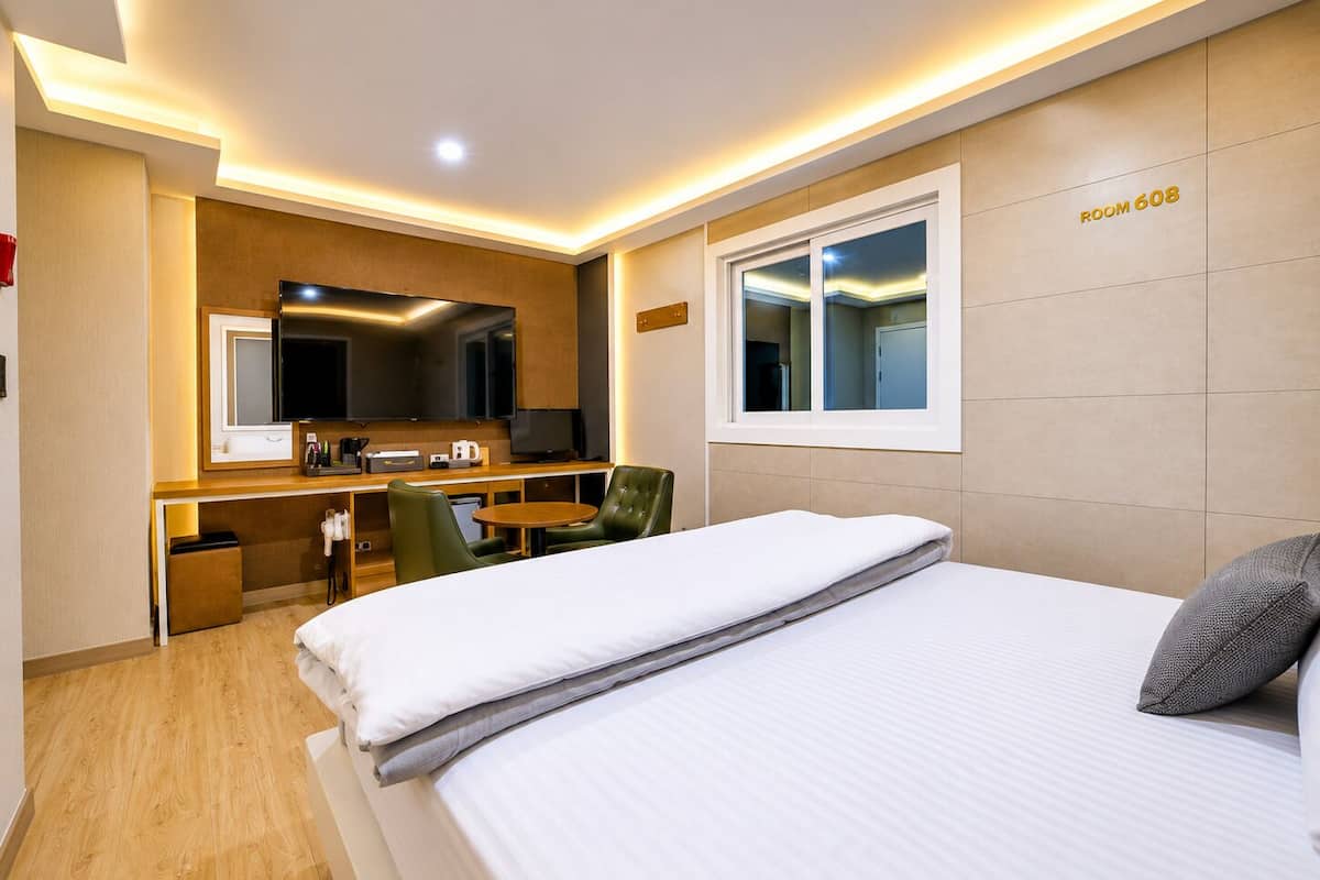 A hotel room with a bed, a desk with a computer, a chair, a TV, and a window.