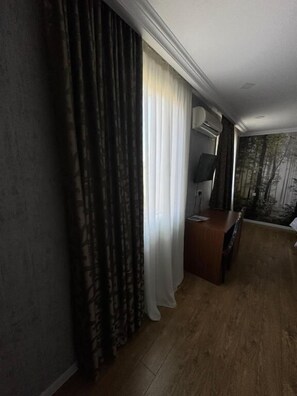 A room with a bed, a desk with a chair, a TV, and a window with curtains. - Hotel Kalanga (Tbilisi)