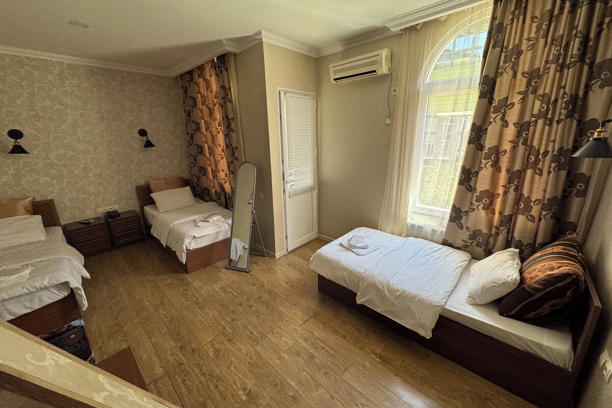 A hotel room with two beds, a mirror, an air conditioning unit, and a window with curtains.