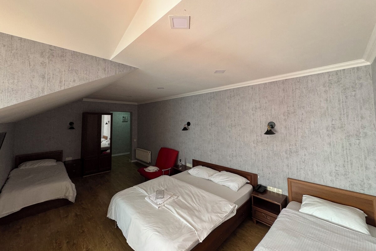 A hotel room with two beds, a red chair, a bedside table with a lamp, and a small window.
