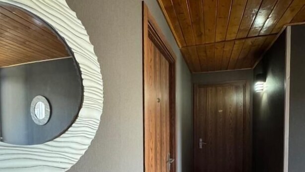 Um corredor com teto de madeira, um ornamento circular na parede e uma porta.