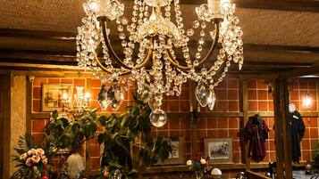 Un candelabro con múltiples velas, un piano, una mesa de comedor, sillas y una zona de bar con un espejo y cuadros enmarcados.