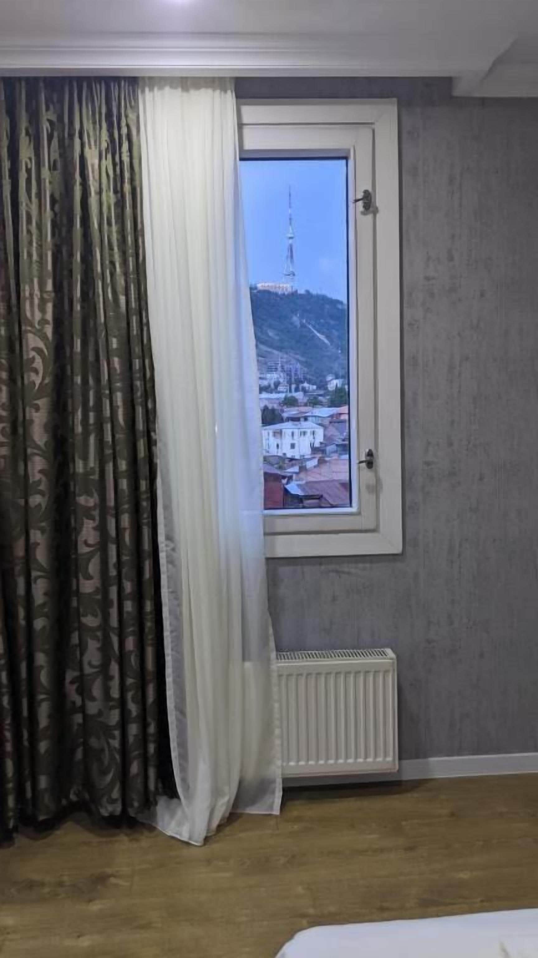 A room with a window, curtains, a radiator, and a bed.