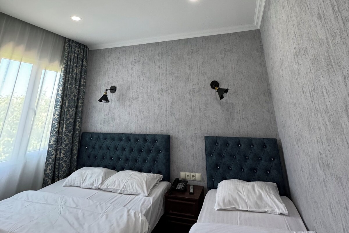 A hotel room with two beds, a large window with curtains, and a textured wall.