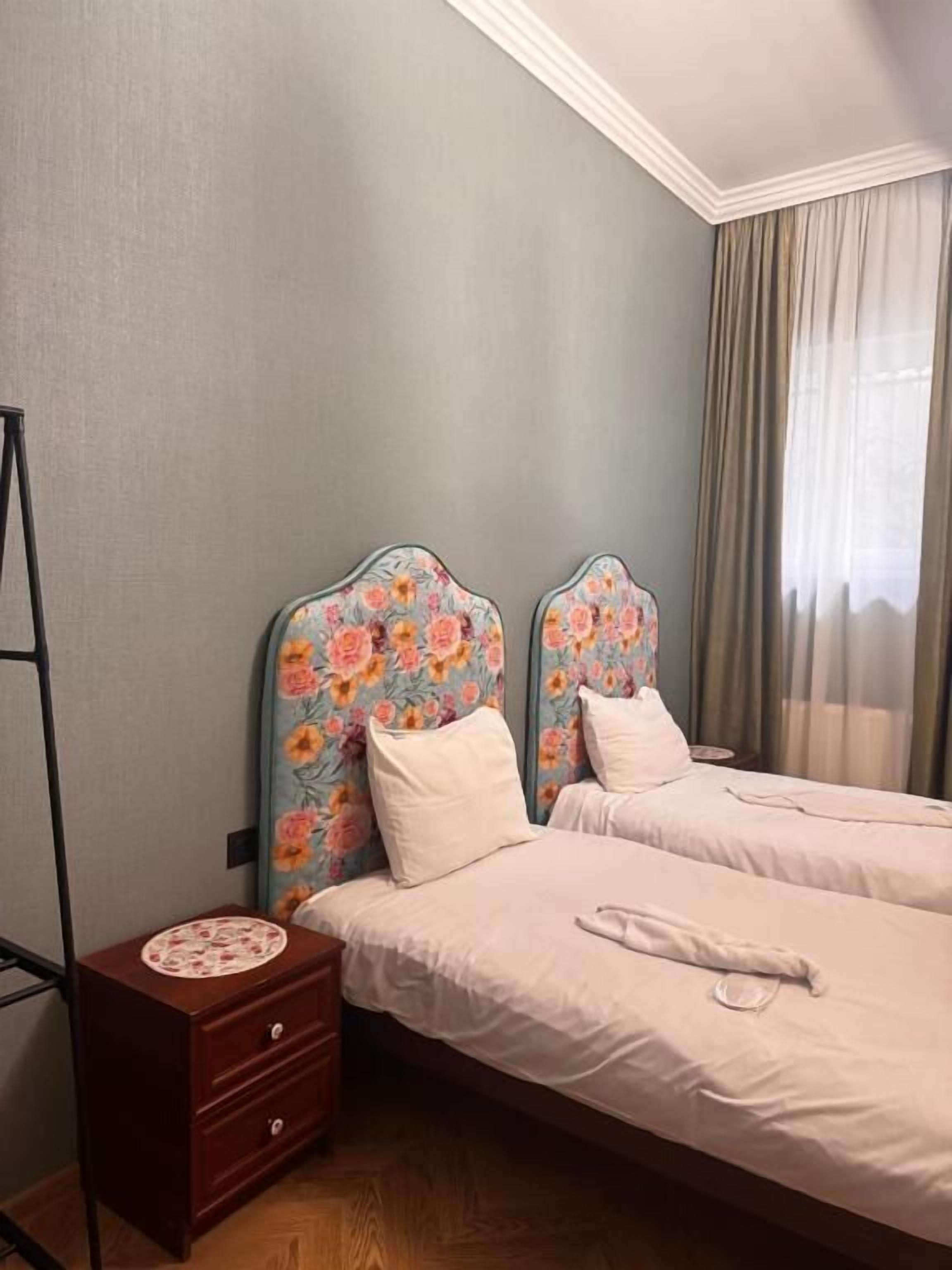 A hotel room with two beds, a nightstand, and a window with curtains.