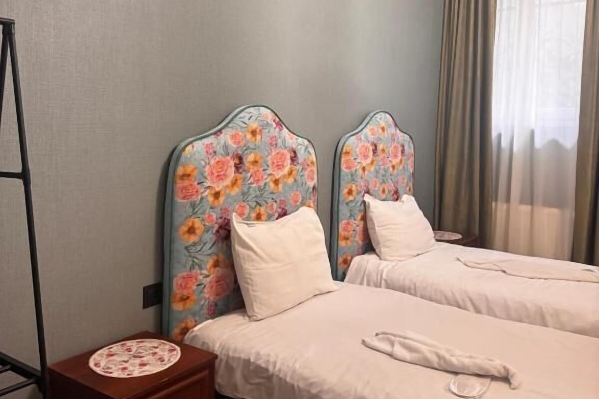 A hotel room with two beds, a nightstand, and a window with curtains.