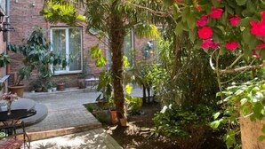 Um jardim com área de pátio, parede de tijolos e lixeira de metal.