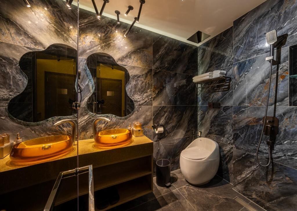 A modern bathroom with a marble wall, a sink, a toilet, and a shower.