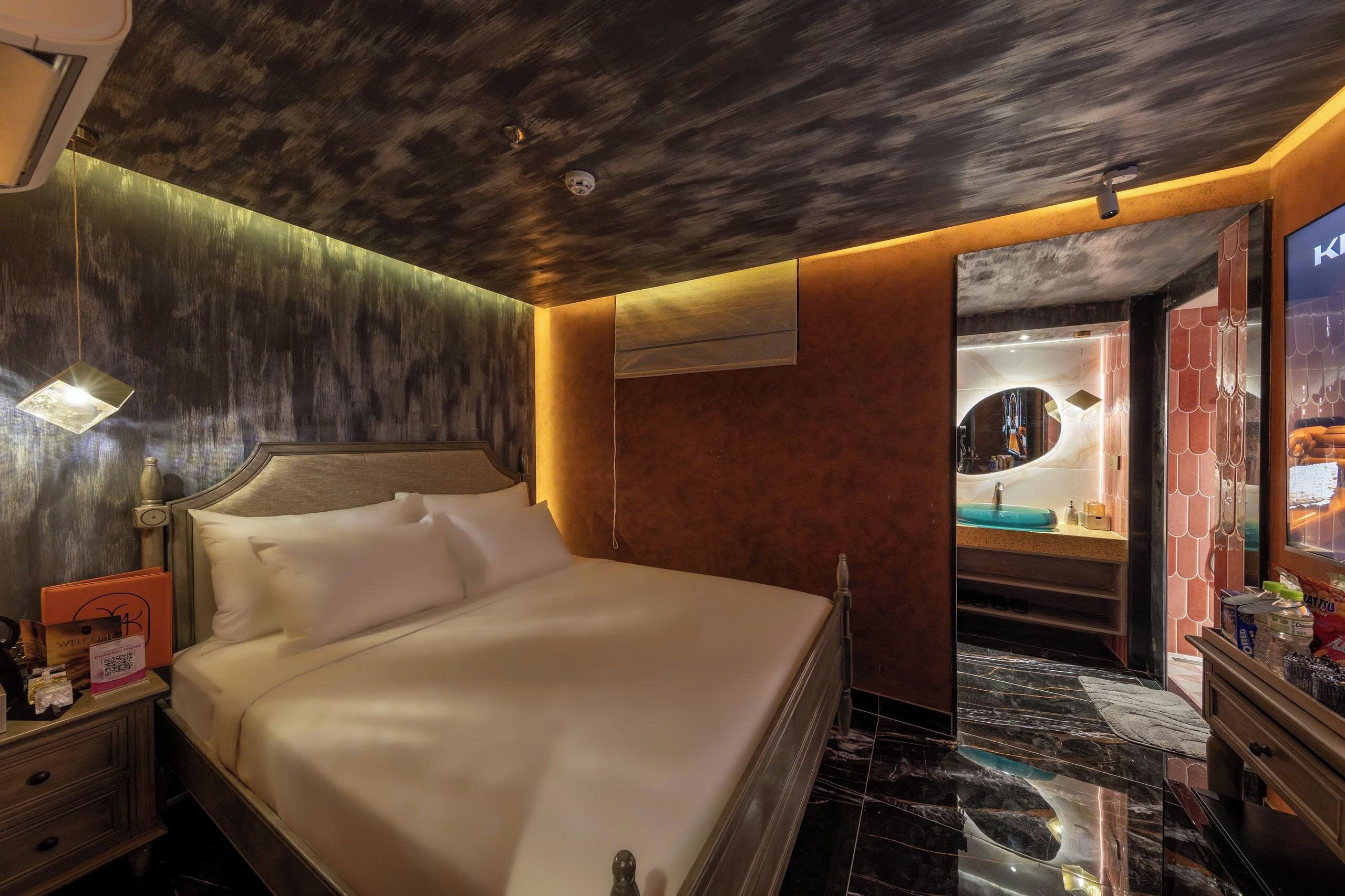 A hotel room with a bed, a nightstand, a mirror, and a bathroom visible through an open door.