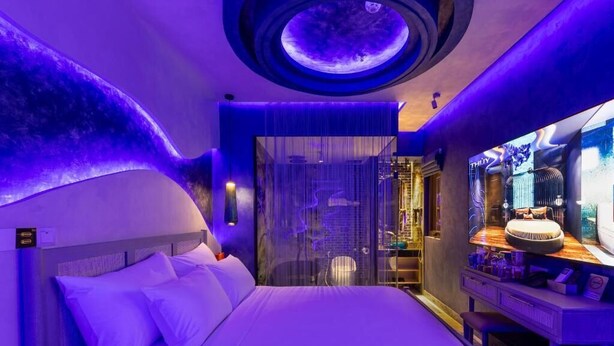 Quarto de hotel moderno com uma cama, toucador com espelho e um detalhe circular no teto.