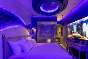 Une chambre d’hôtel moderne comprenant un lit, une coiffeuse avec un miroir et un élément décoratif circulaire au plafond.