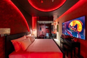 Una habitación de hotel moderna con una cama grande, un televisor y techo con iluminación roja.