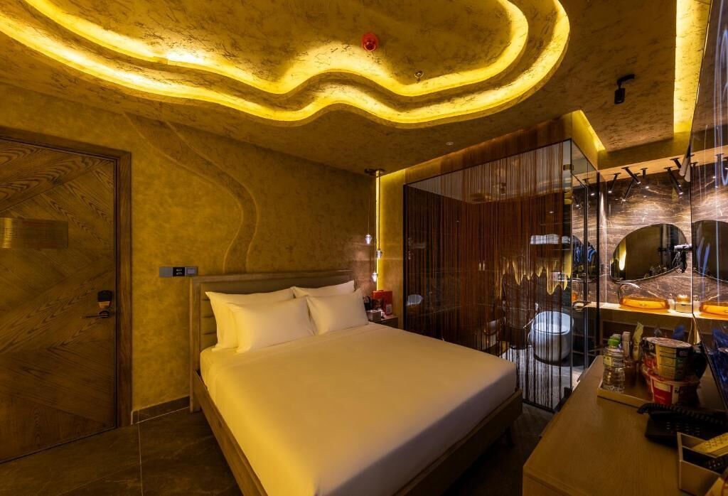 A modern hotel room with a large bed, a wooden door, a vanity with a mirror, and a curved ceiling design.
