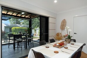 Zona pranzo con tavolo imbandito per quattro persone, una porta vetrata che dà sull'esterno e una foglia decorativa appesa al muro.