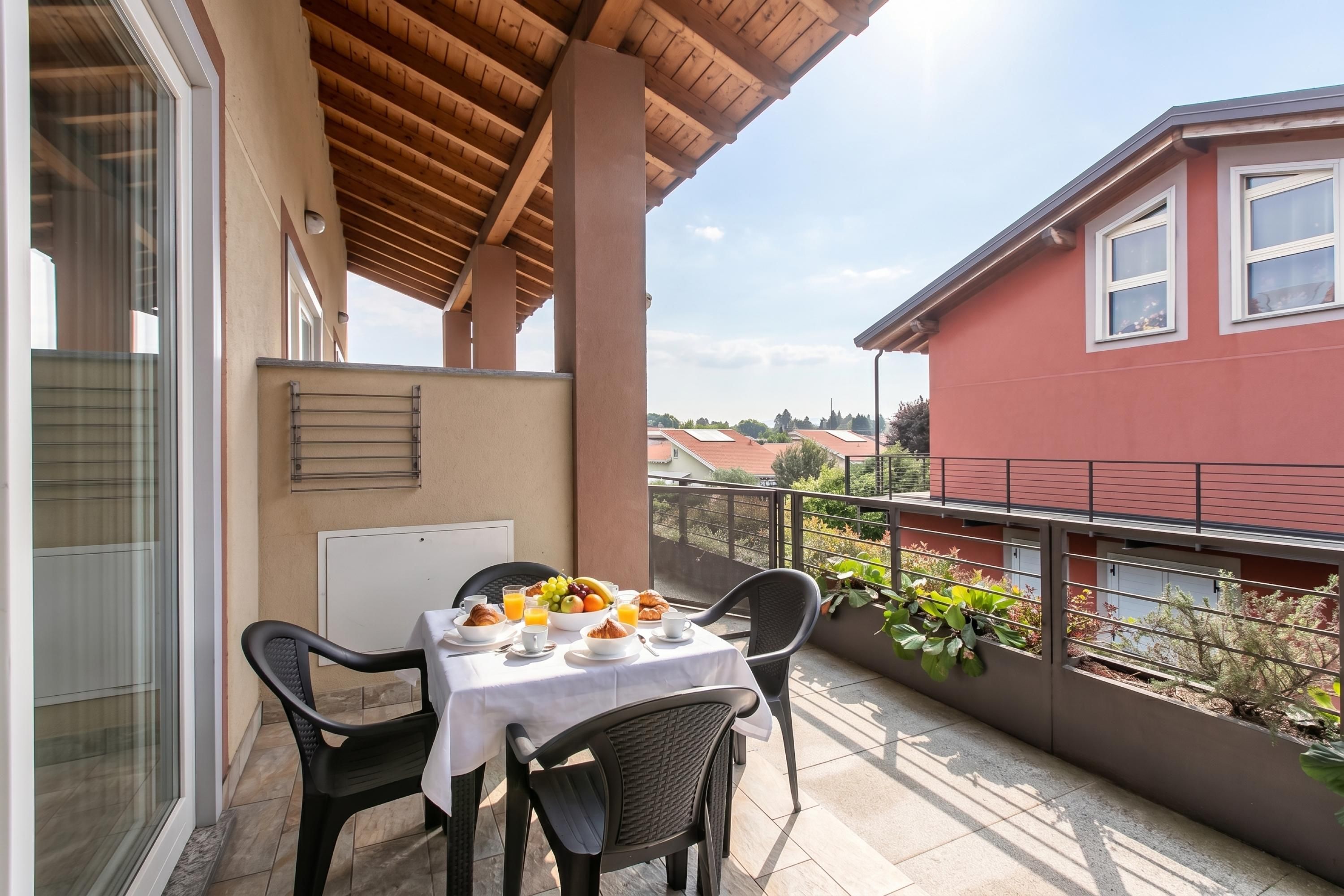 Un balcó amb una taula preparat per esmorzar, cadires i vista d'un edifici vermell.