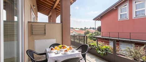 A balcony with a table set for breakfast, chairs, and a view of a red building.