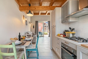 A kitchen with a stove, oven, and dining area with chairs and a table. - Cozy Ispra Residence With Terrace, Near Beach Air-con (Ispra)