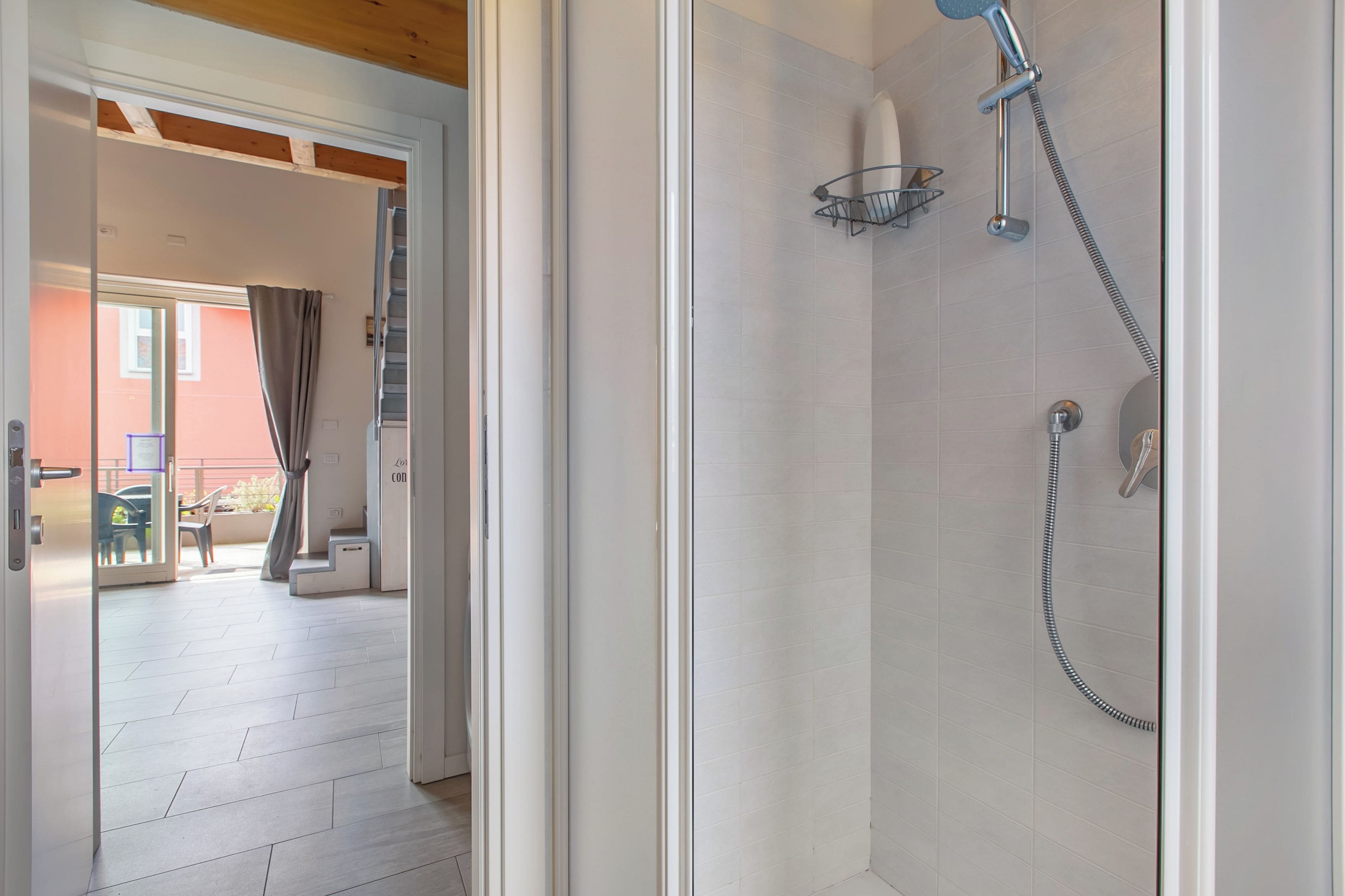 A shower with a handheld showerhead, a wall-mounted towel rack, and a glass door leading to an outdoor area with a table and chairs.