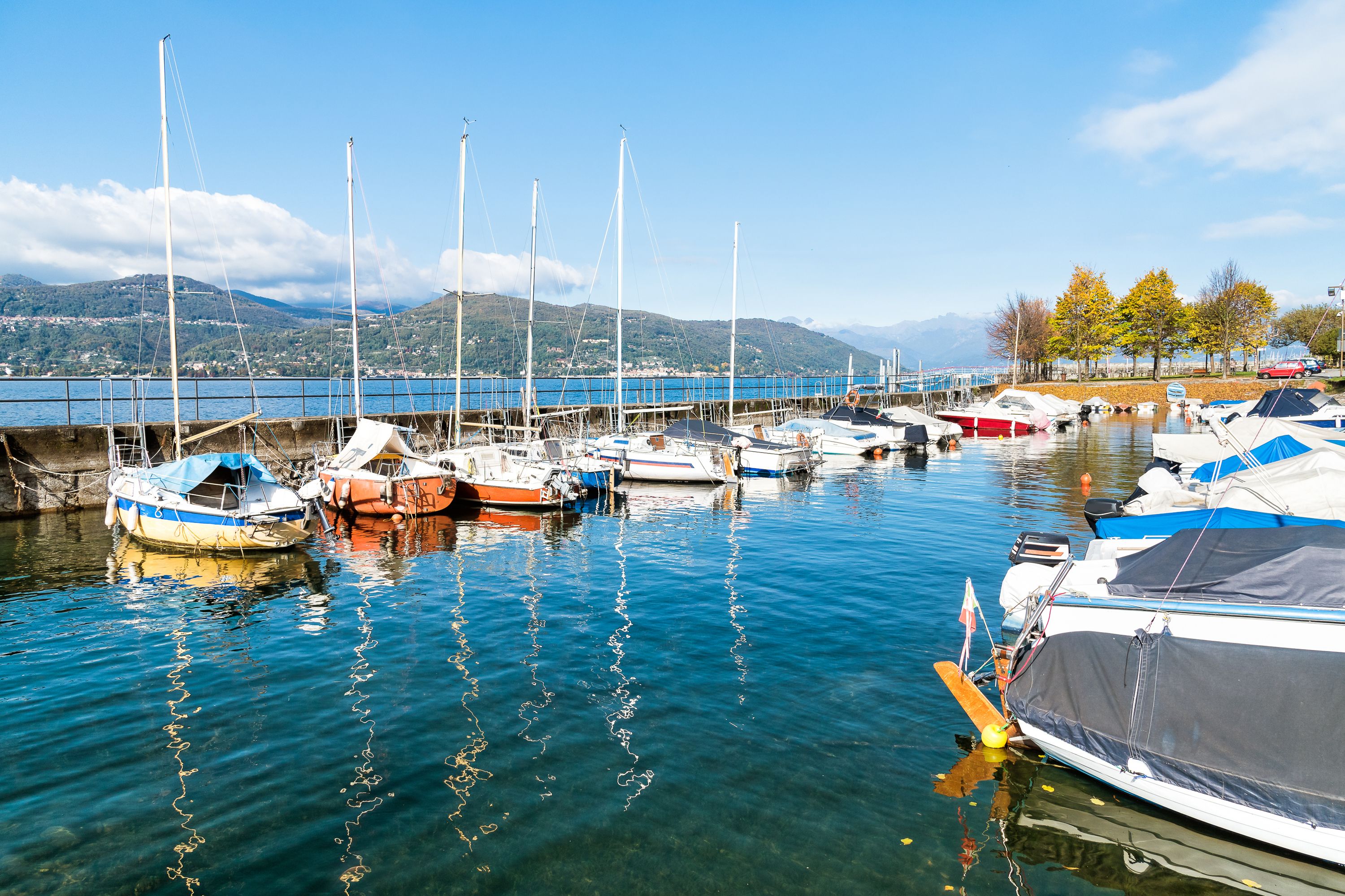 A marina with boats docked, calm water, and a mountainous backdrop.