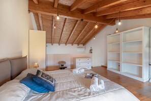 A bedroom with a wooden ceiling, a bed with pillows, a nightstand, a dresser, and a white shelving unit. - Cozy Ispra Residence With Terrace, Near Beach Air-con (Ispra)