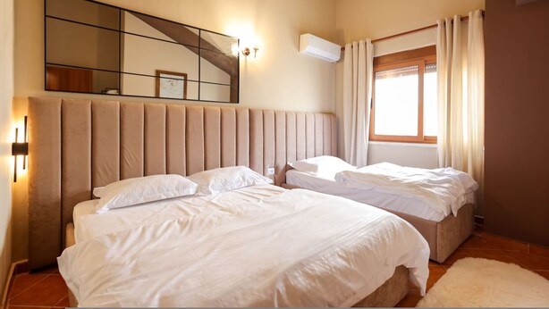 Una camera da letto con due letti, un grande specchio, un condizionatore d'aria e una finestra con tende.