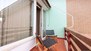 Un balcone con due poltrone in vimini, una porta in vetro e un muro in mattoni.