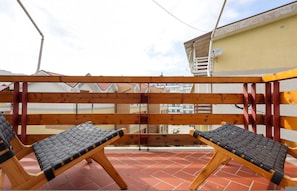 Eine Dachterrasse mit zwei Liegestühlen, einer Holzpergola und Blick auf Gebäude im Hintergrund.