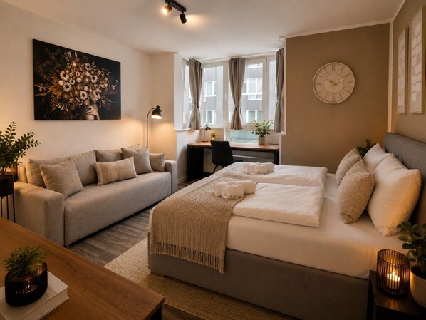 A hotel room with a bed, a sofa, a desk, and a large window with curtains.