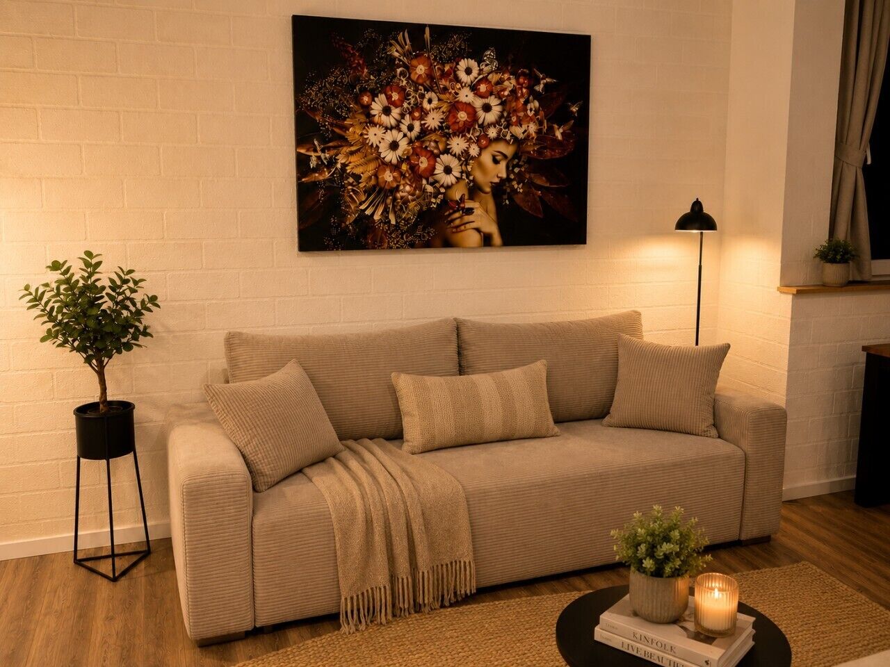 Ein Wohnzimmer mit einem beigen Sofa, einer schwarzen Stehlampe, einem Topf mit Pflanze und einem Bild an der Wand.