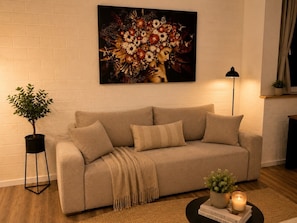Un salon avec un canapé beige, un lampadaire noir, une plante en pot et un tableau accroché au mur.