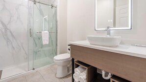 A modern bathroom with a glass shower enclosure, a white toilet, a large mirror, and a white sink. - Newly Renovated Hotel - 2 Bedroom Suites with Kitchen in beautiful Columbia (Columbia)