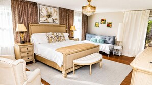 Ein Schlafzimmer mit einem großen Bett, Nachttischen, einem Sessel, einer Bank, einer Chandelier und Kunstwerken an den Wänden.