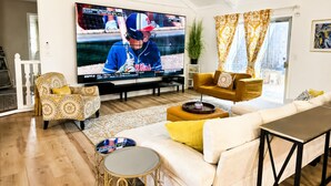 Ein Wohnzimmer mit einem großen Flachbildfernseher, einem Sofa, einem Couchtisch und einem gemusterten Sessel.
